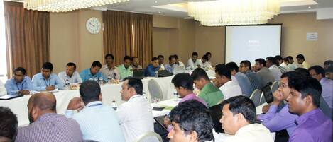 A conference room with a long table, attendees, laptops, and a projector screen.