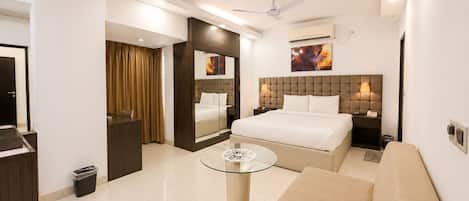 Habitación de hotel con cama, sofá, mesa de centro de vidrio, ventilador de techo y aire acondicionado de pared.