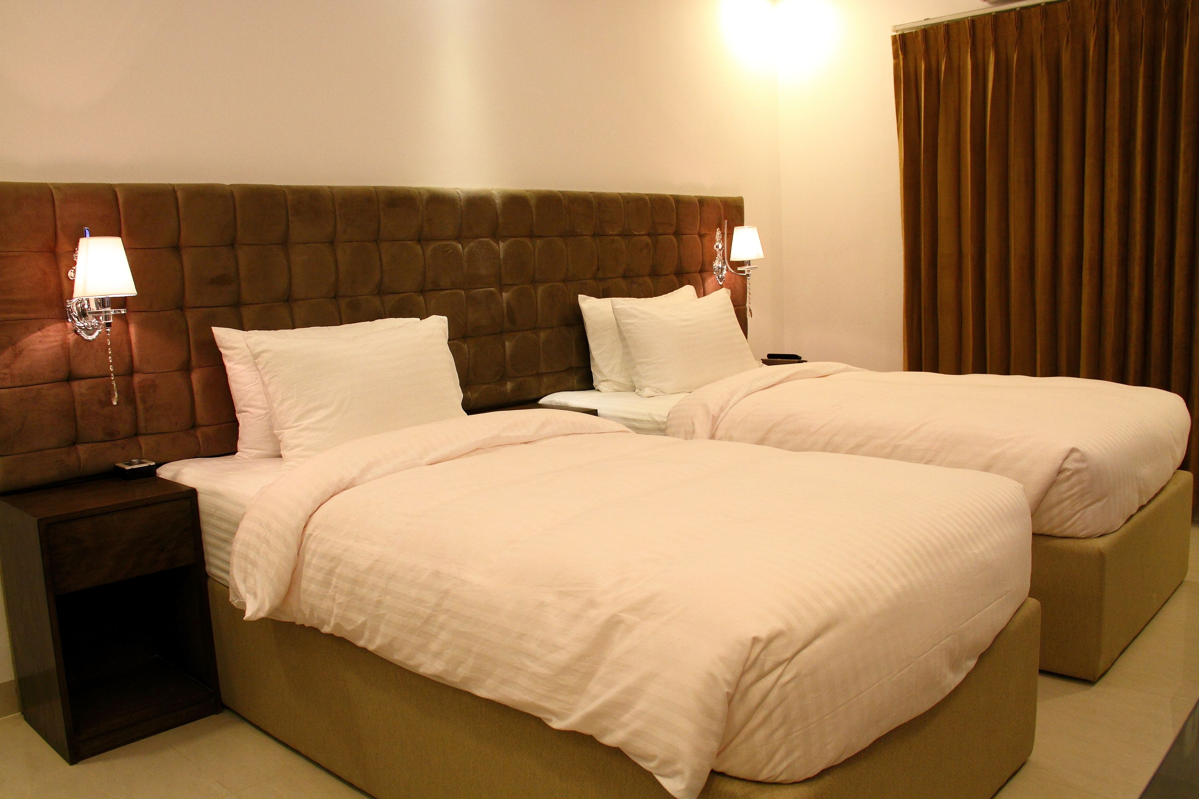 A double bed with a tufted headboard, two bedside tables with lamps, and a large window with curtains.