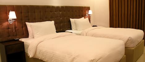 A double bed with a tufted headboard, two bedside tables with lamps, and a large window with curtains.