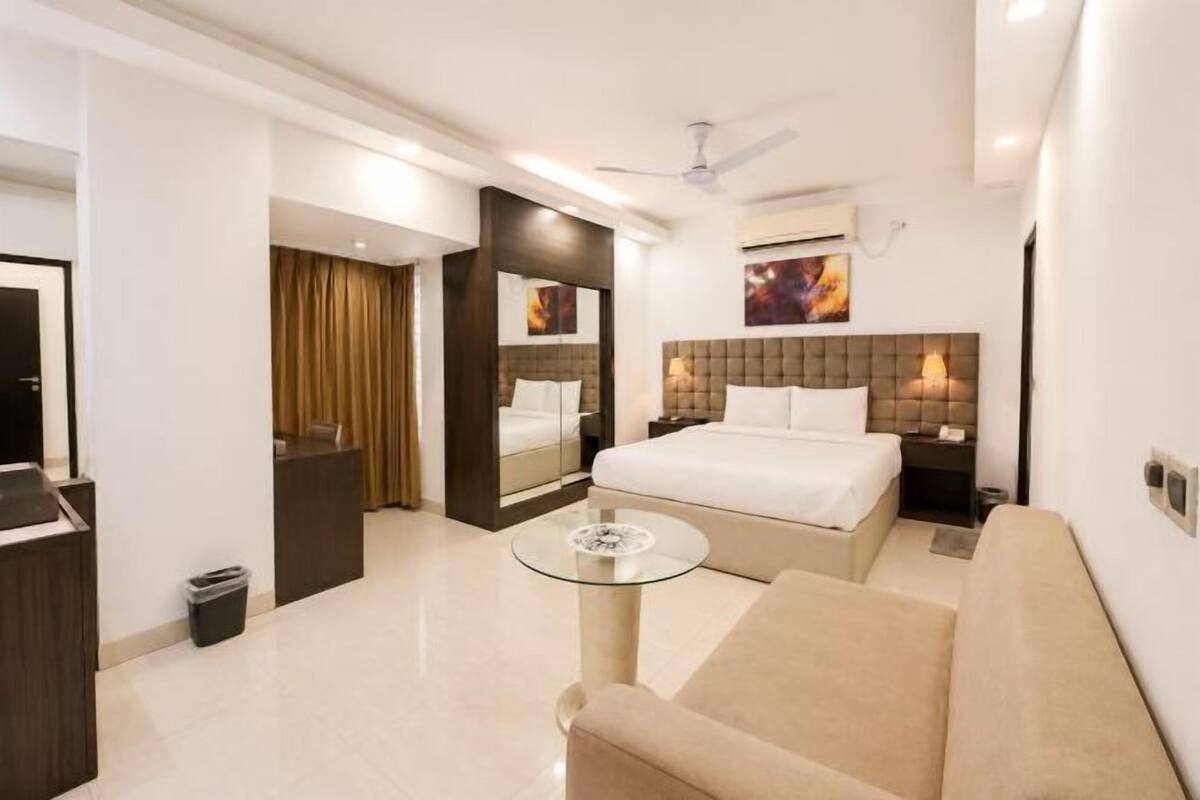 A hotel room with a bed, a sofa, a glass coffee table, a desk, and a mirror.