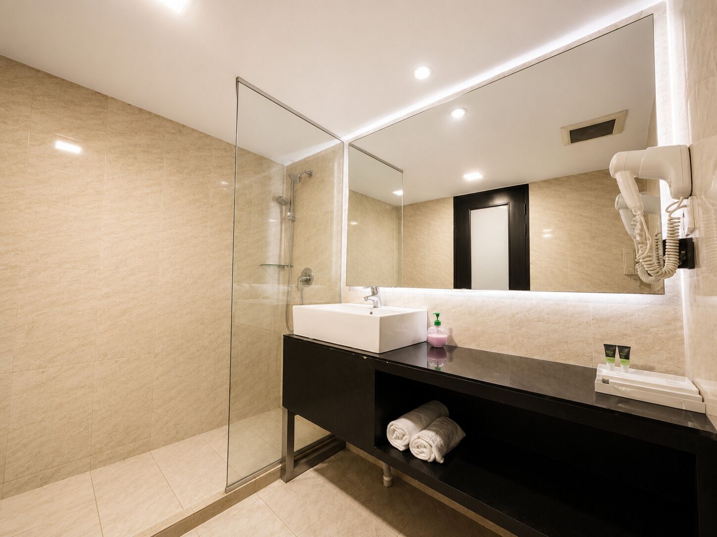 A modern bathroom with a glass shower enclosure, a white sink, a black vanity, and a large mirror.