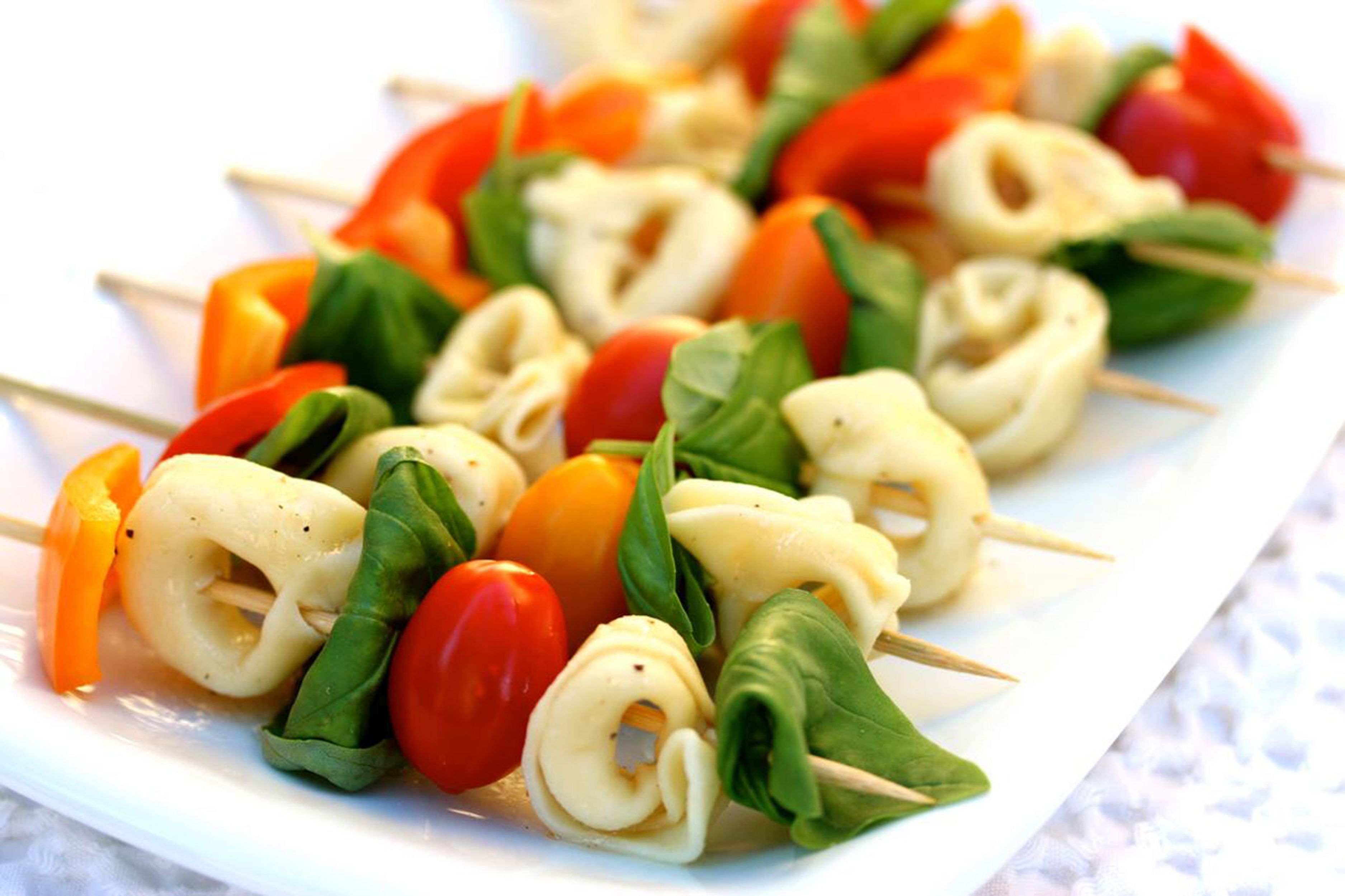 Een bord met spiesjes groente, tomaten, spinazie en kaas.