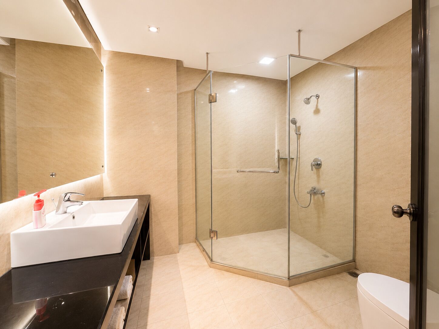 Un baño moderno con ducha de vidrio, un lavabo blanco y un mueble de tocador negro.