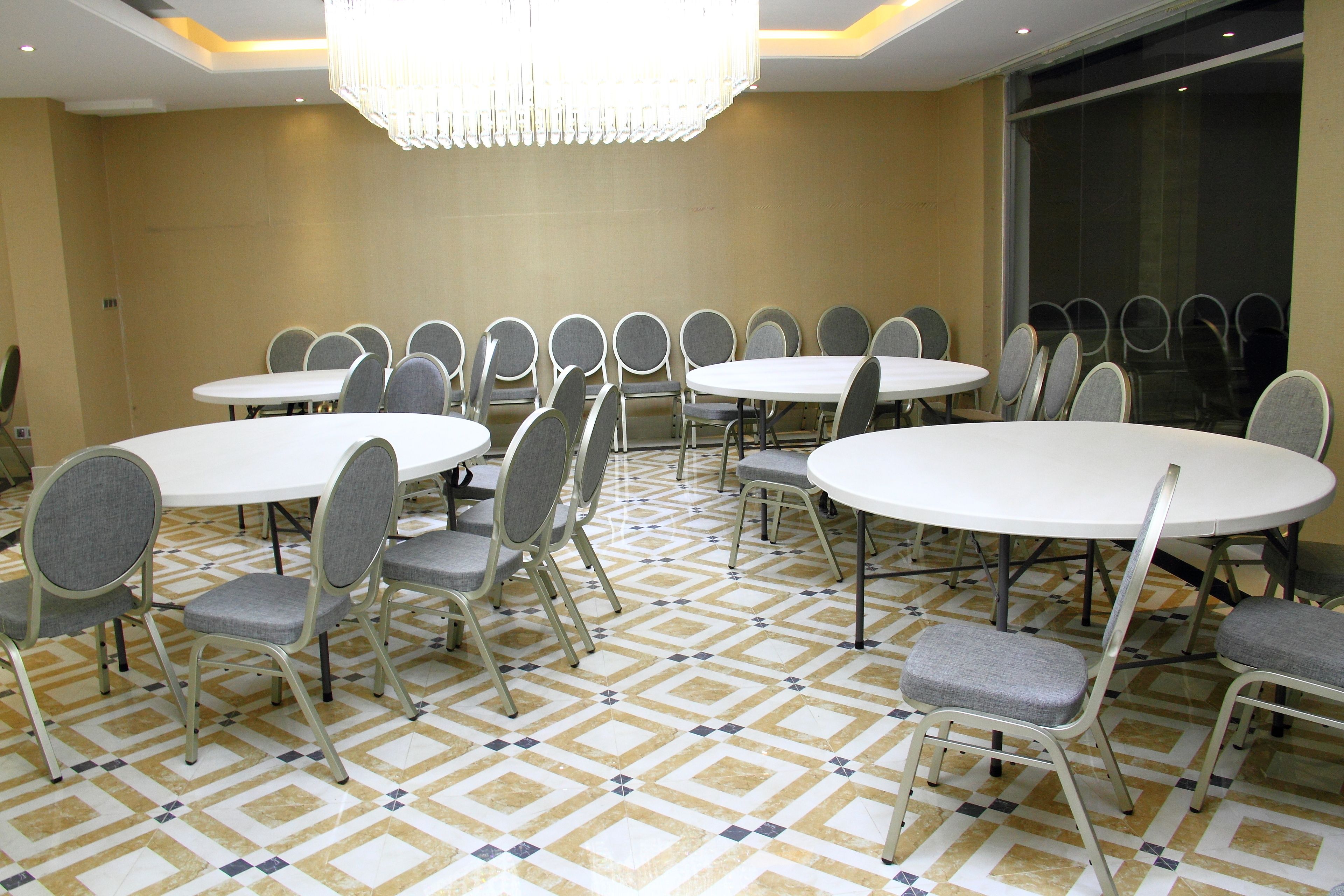 A conference room with multiple round tables and grey upholstered chairs, arranged in a U-shape.