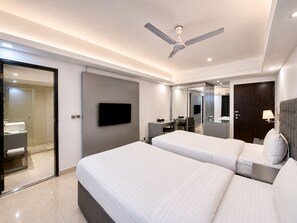 A modern hotel room with two beds, a flat-screen TV, a desk, a chair, a mirror, a ceiling fan, and a door. - Blossom Hotel Dhaka (Dhaka)