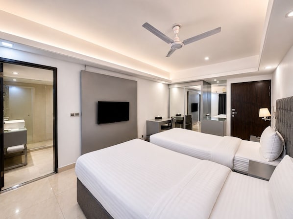 Una habitación de hotel moderna con dos camas, un televisor de pantalla plana, un escritorio, una silla, un espejo, un ventilador de techo y una puerta.