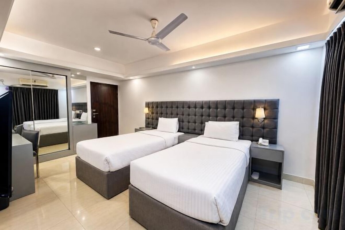 Habitación de hotel con dos camas, un ventilador de techo, un espejo grande y un televisor.