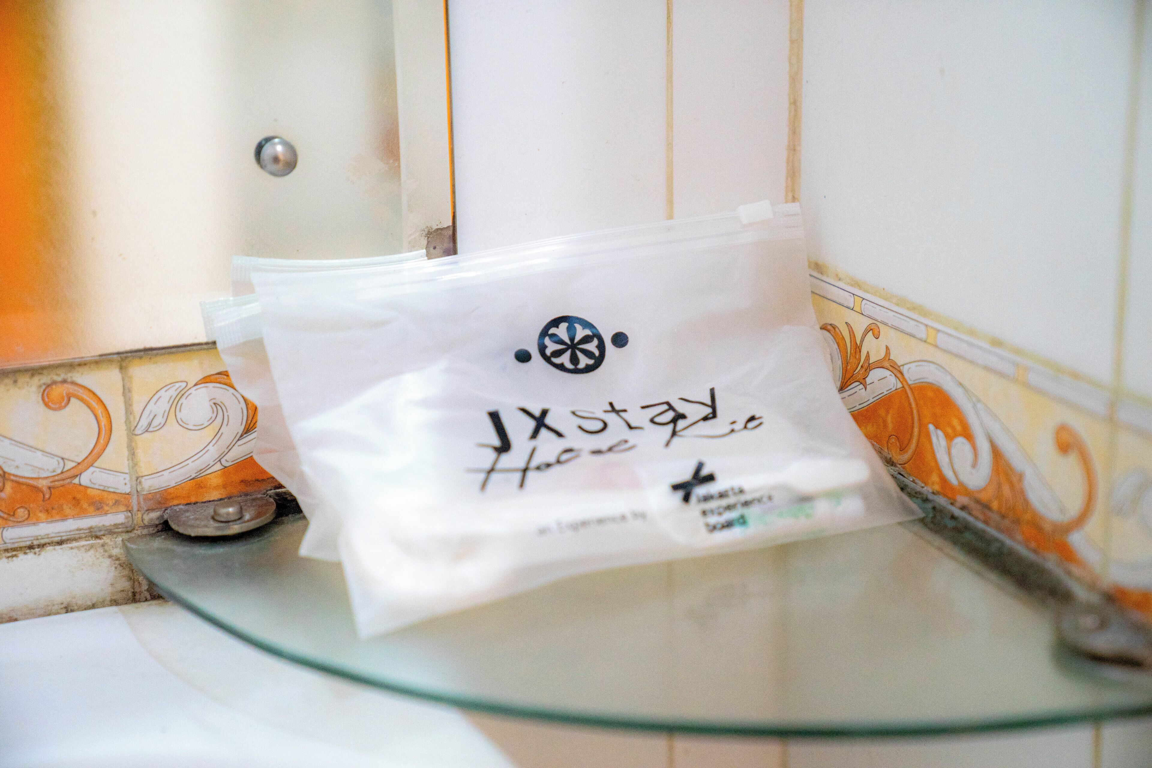Ein Badezimmer mit einer Glasabtrennung, einem weißen Mülleimer und einer weißen Tasche mit Aufschrift.