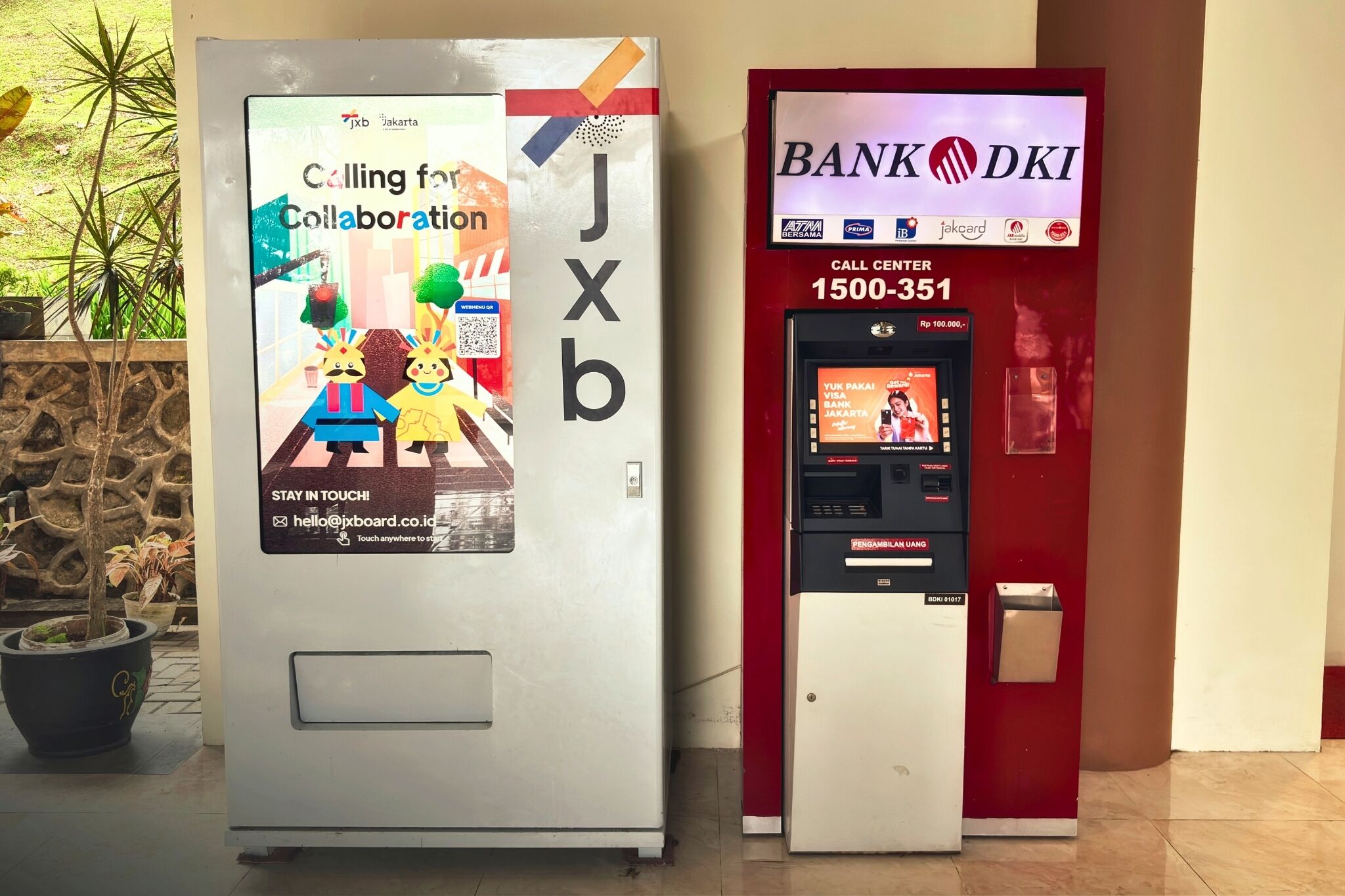 Un quiosco JXB con un anuncio colorido y un cajero automático de BANK DKI.