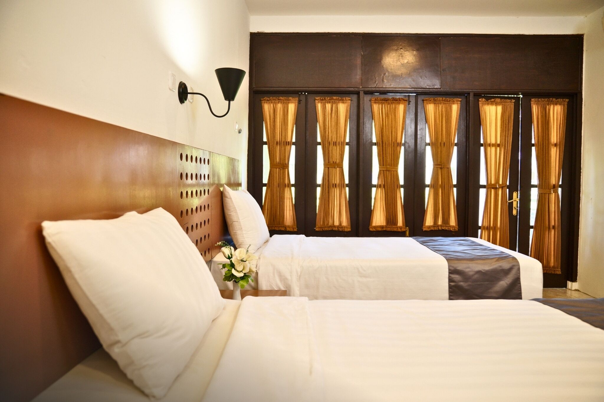 A hotel room with two beds, a headboard, a wall-mounted light fixture, and a window with curtains.