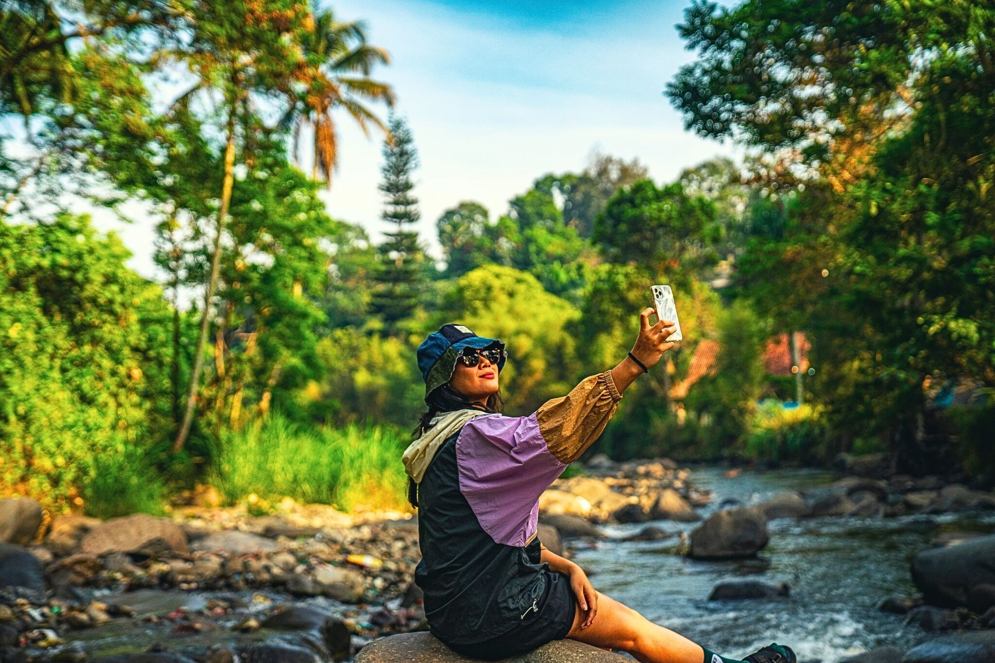 Une personne prenant un autoportrait dans un environnement naturel, avec une rivière et de la végétation en arrière-plan.