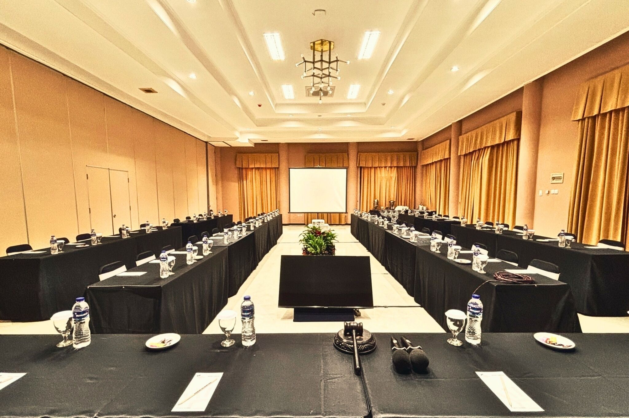 A conference room with long tables, water bottles, and a projector screen.