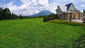 A large house with a sloped roof, surrounded by a green field and trees.
