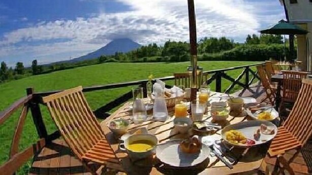 An outdoor dining area with a table set for breakfast, overlooking a mountainous landscape.