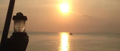 Ein Sonnenuntergang über ruhigem Meer mit einem entfernten Boot und einem Leuchtturm im Vordergrund.