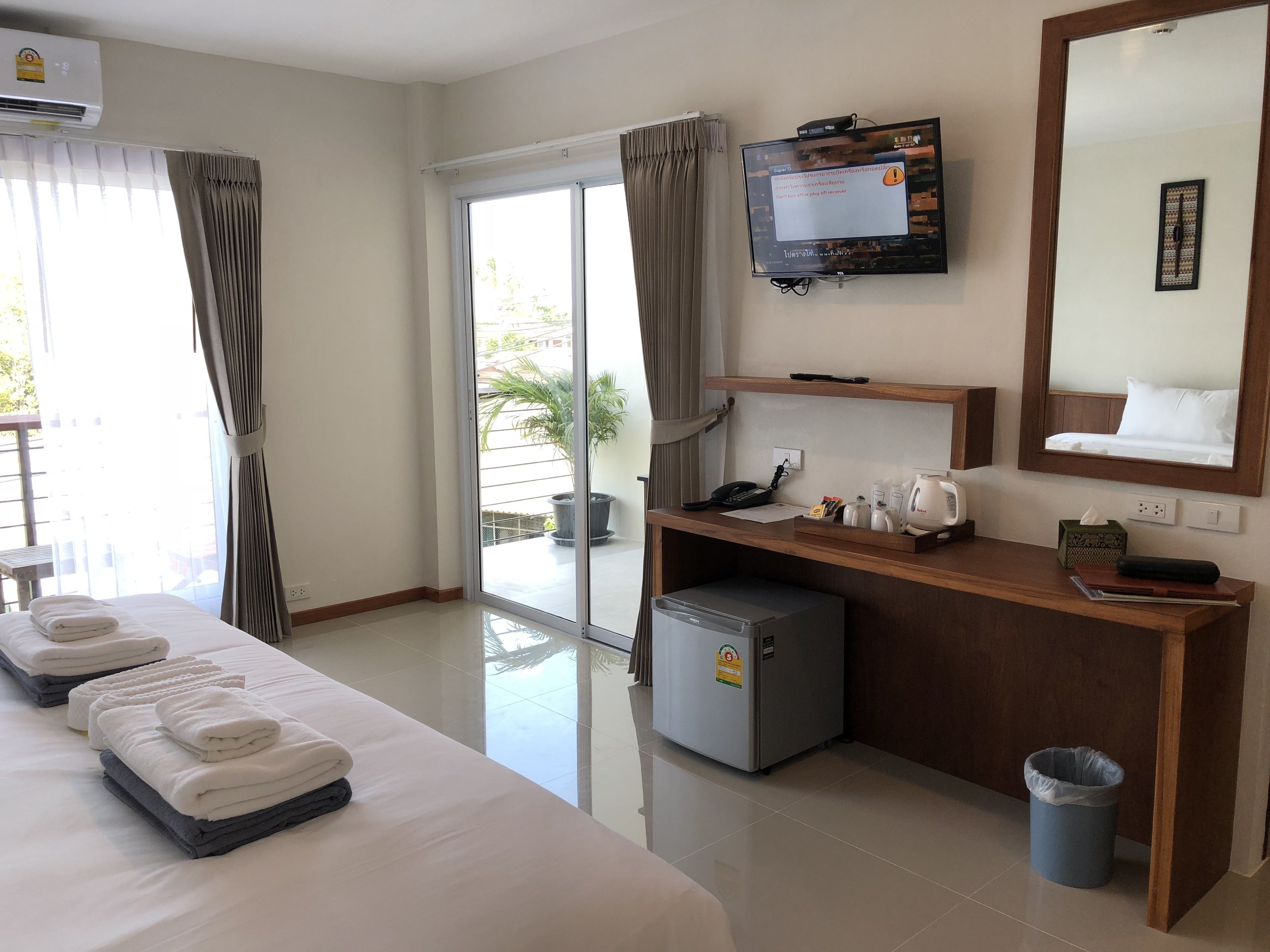 A hotel room with a bed, a desk with a telephone, a small refrigerator, a trash can, a television, and a window with curtains.