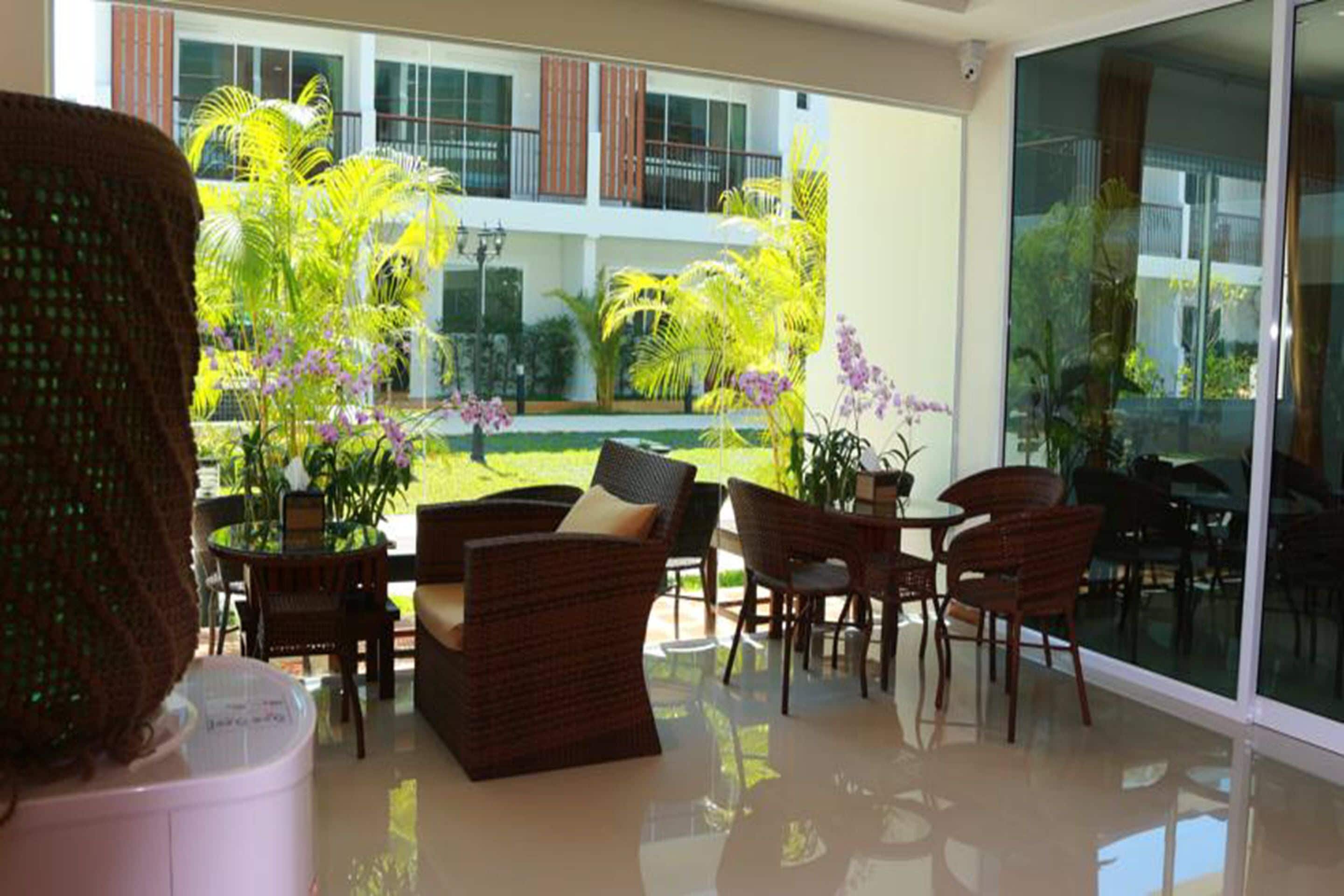 A modern indoor space with wicker furniture, a glass table, and a view of a lush garden and building exterior.
