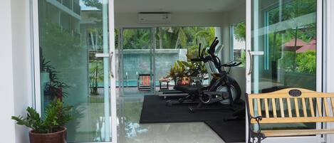 Entrada de gimnasio con equipo de ejercicio, un banco y una planta en maceta.