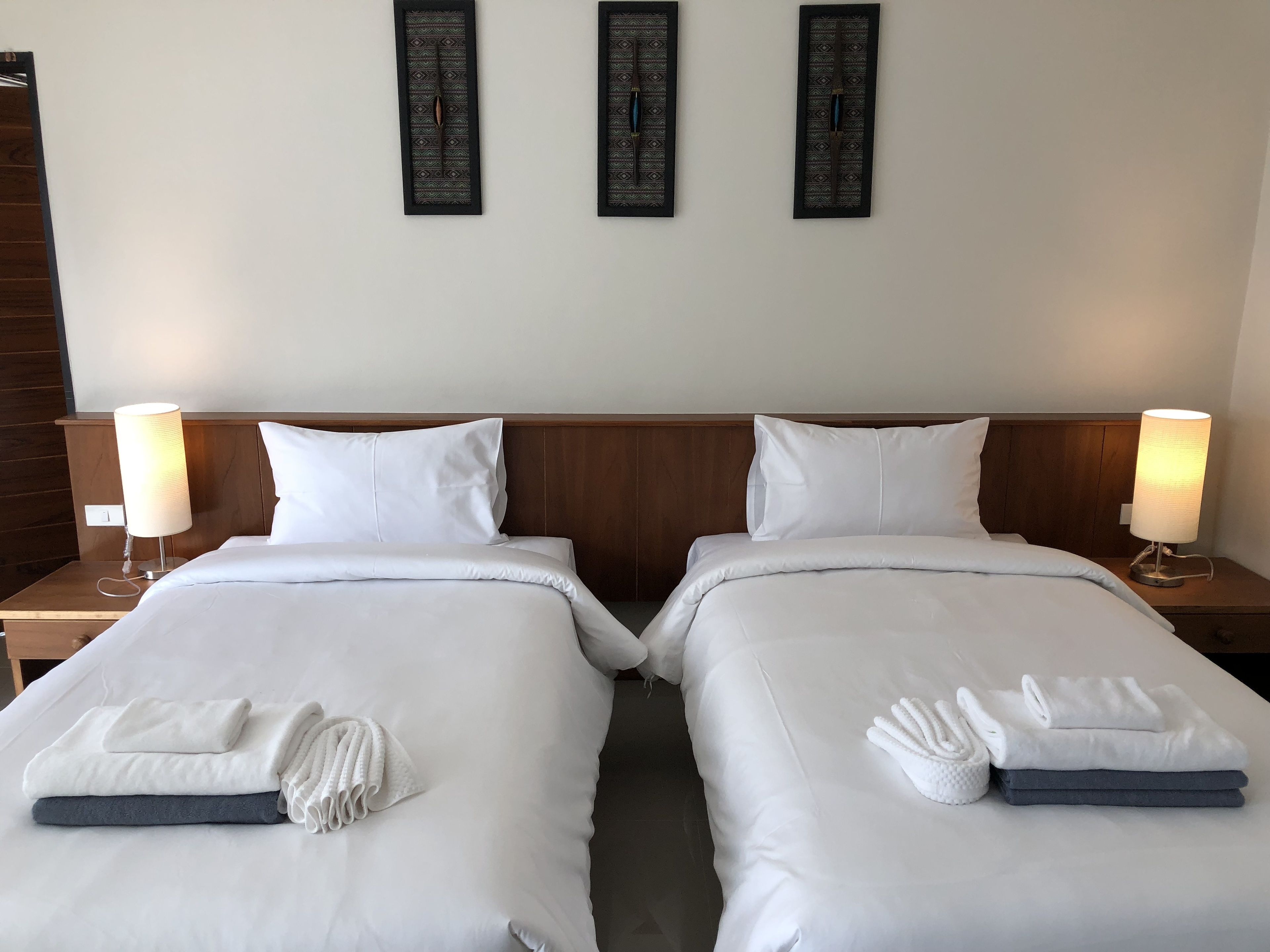 Habitación de hotel con dos camas individuales, ropa de cama y toallas blancas. Hay dos mesitas de noche con lámparas. Las paredes tienen tres adornos decorativos.