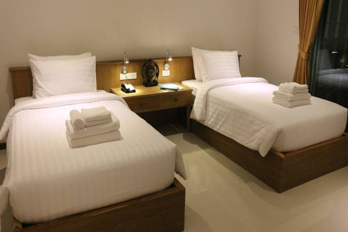 A hotel room with two beds, a nightstand with lamps, and a window with curtains.