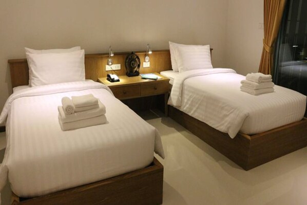 Habitación de hotel con dos camas, una mesita de noche con lámparas y una ventana con cortinas.