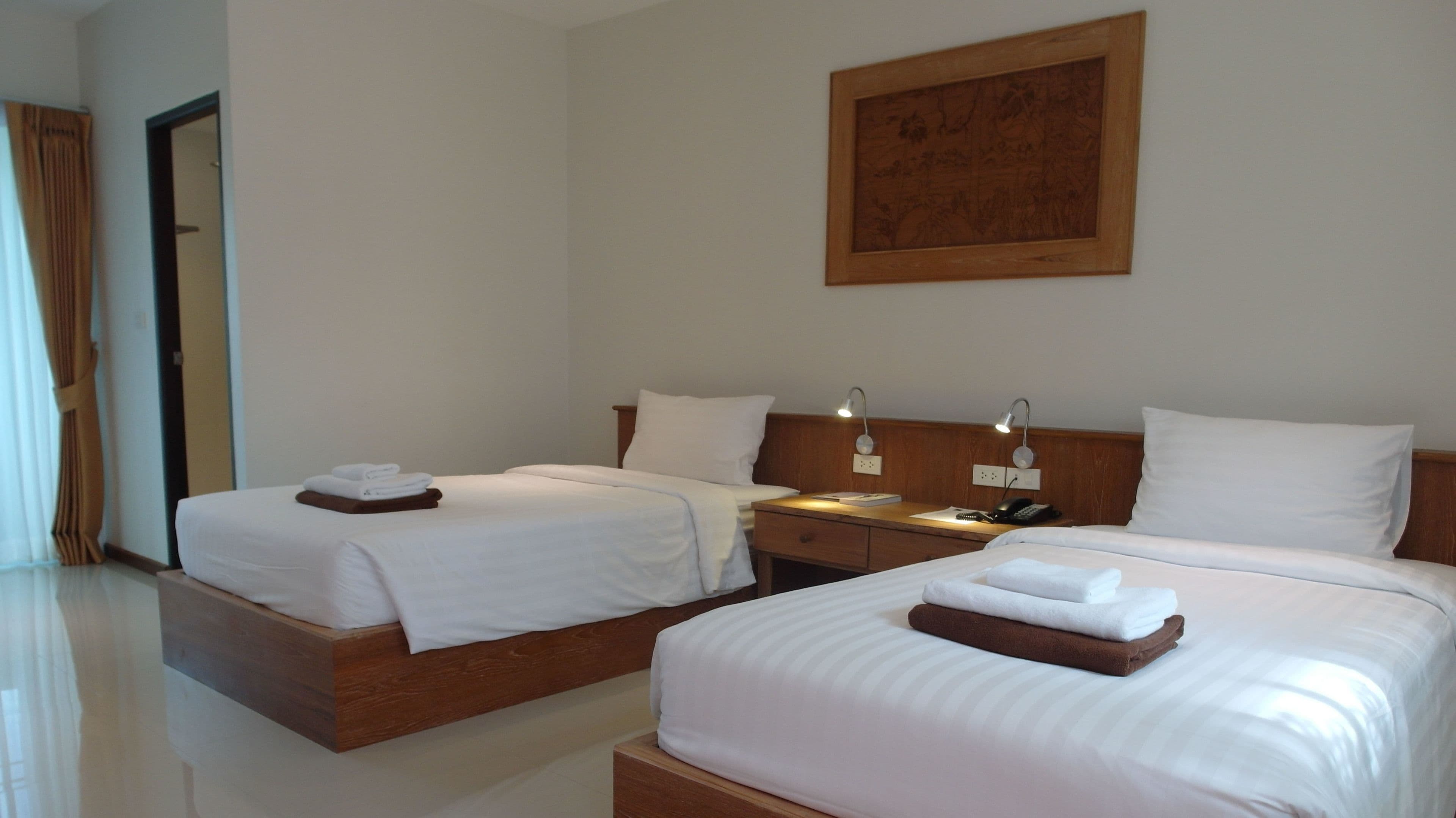 A hotel room with two beds, a wooden headboard, bedside tables with lamps, and a framed picture on the wall.
