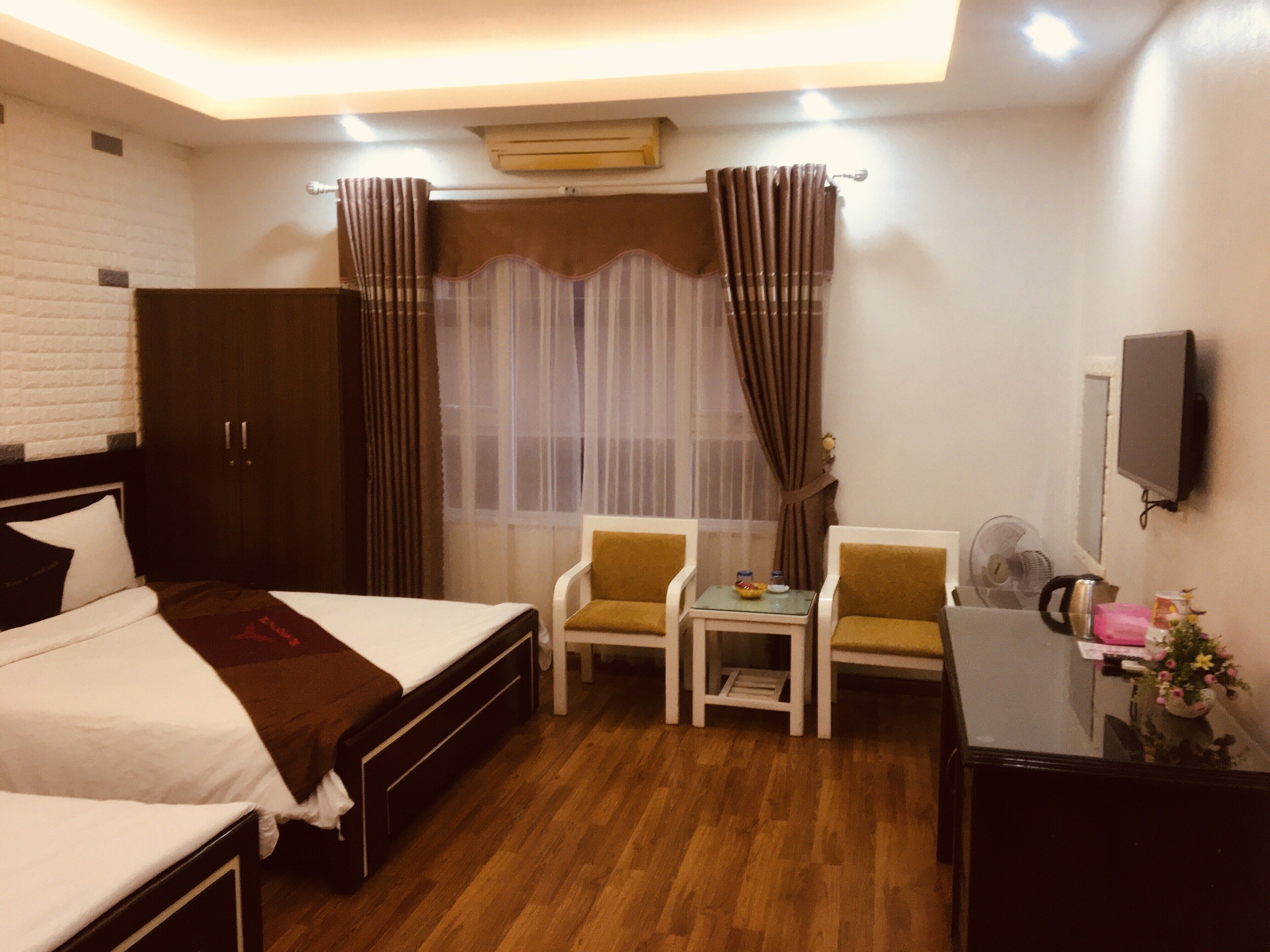A hotel room with a bed, a desk, two chairs, a television, and a window with curtains.