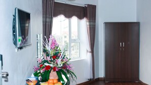 Een kamer met een houten kast, een bureau met een bloemenvaas en fruit, een garderobe en een raam met gordijnen.