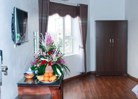Quarto com armário de madeira, escrivaninha com vaso de flores e frutas, guarda-roupa e janela com cortinas.