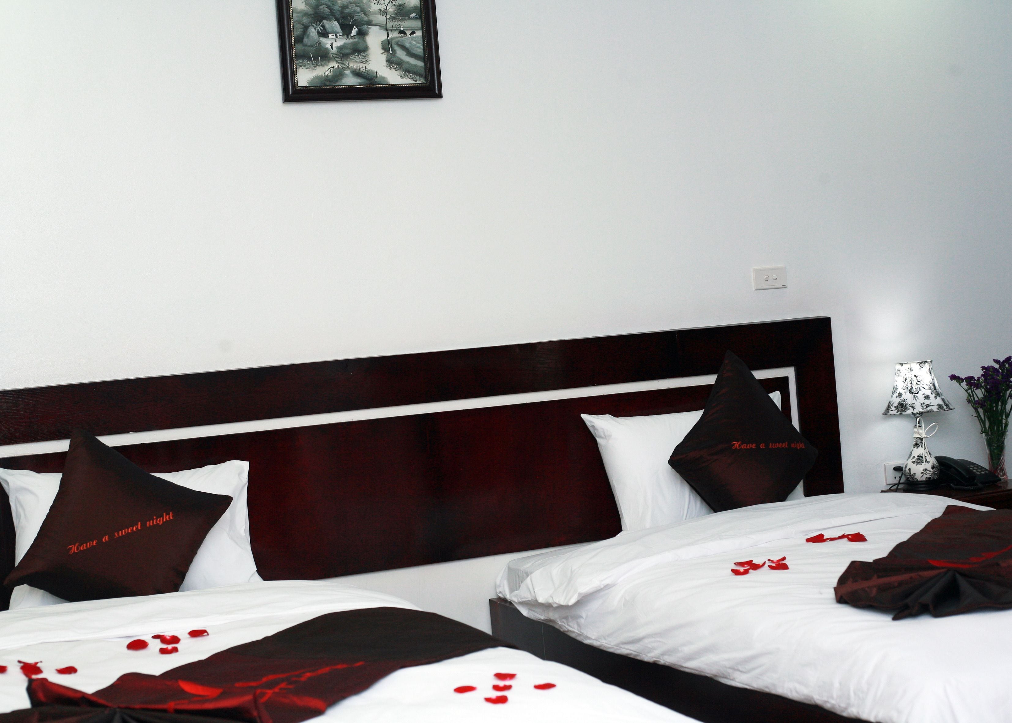 A hotel room with two beds, dark wood headboard, white bedding, and rose petals on the beds.
