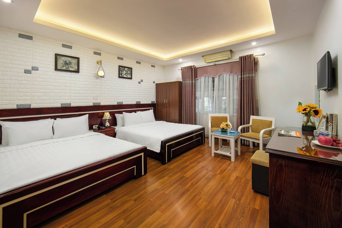 Quarto de hotel com duas camas, uma escrivaninha, uma cadeira, uma televisão e uma janela com cortinas.