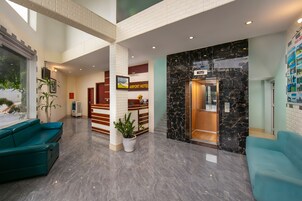 Um saguão de hotel com balcão de recepção, escada e áreas de estar.