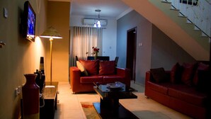 A living room with a red sofa, a coffee table, a TV, and a staircase. - Crystal Court Lekki (Lekki)