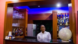 A bar area with a bartender, shelves of liquor bottles, and a decorative sphere. - Crystal Court Lekki (Lekki)