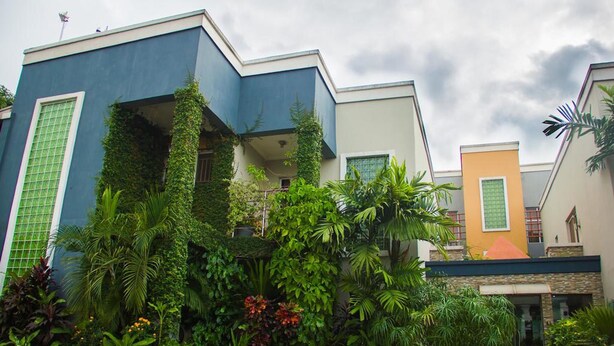A modern building with a blue and beige facade, surrounded by lush greenery and tropical plants. - Crystal Court Lekki (Lekki)