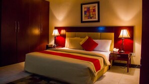 A hotel room with a large bed, two bedside tables, a nightstand, a wardrobe, and a framed artwork on the wall. - Crystal Court Lekki (Lekki)