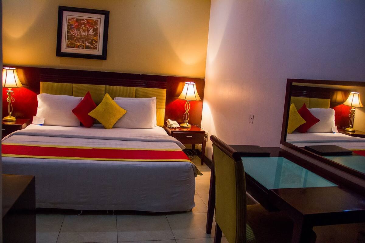 A hotel room with a large bed, two bedside tables with lamps, a mirror, and a framed picture on the wall.