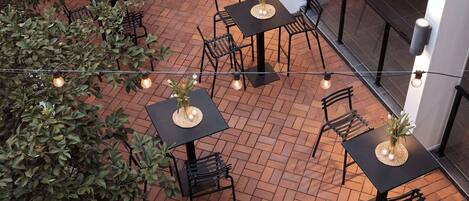 A patio area with tables and chairs, string lights, and potted plants.