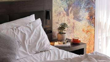 A neatly made bed with white linens, a brown throw blanket, and a bedside table with a potted plant, a cup, and a pair of sunglasses.