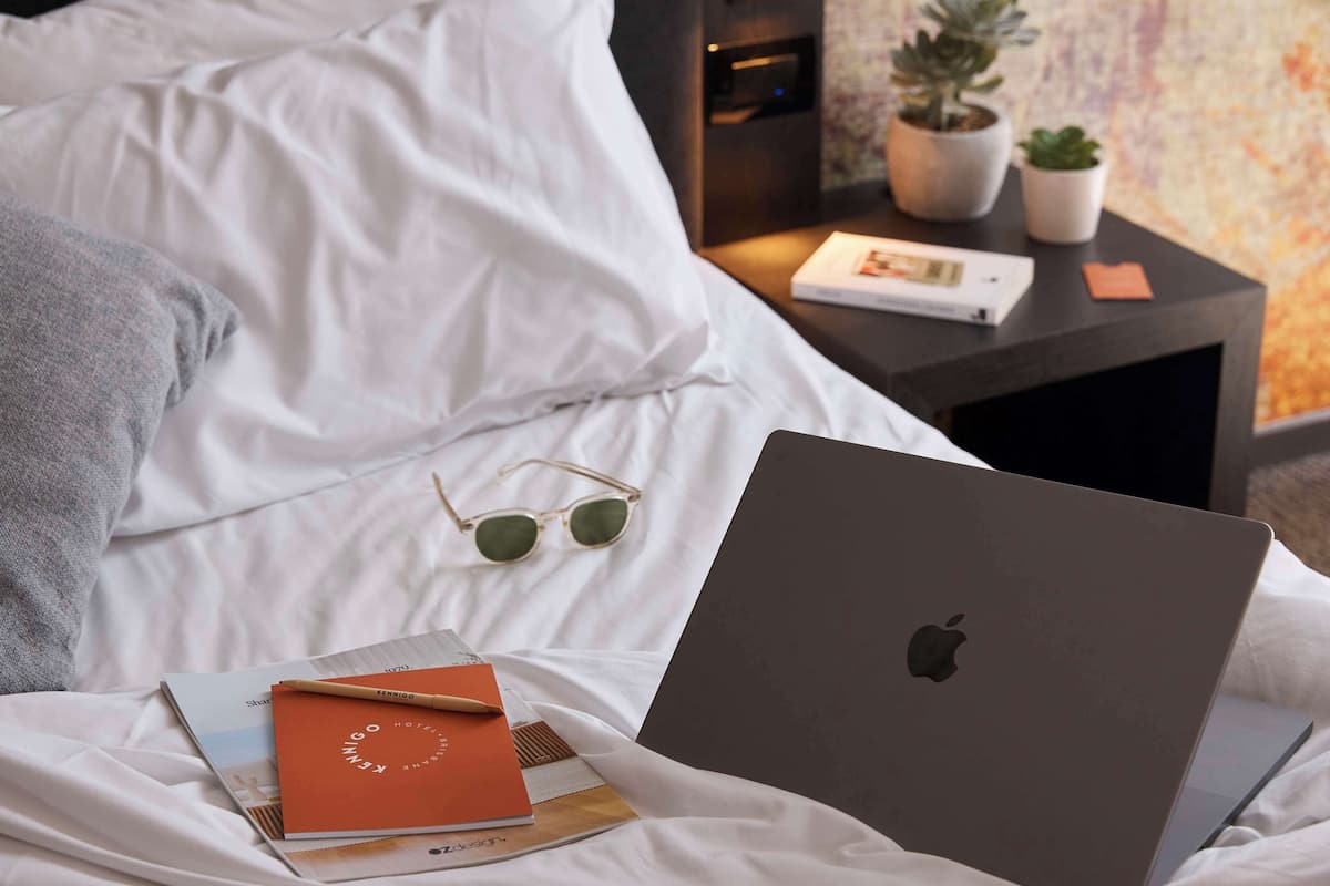 Ein Bett mit einem Laptop, einer Sonnenbrille und einem Notizbuch.