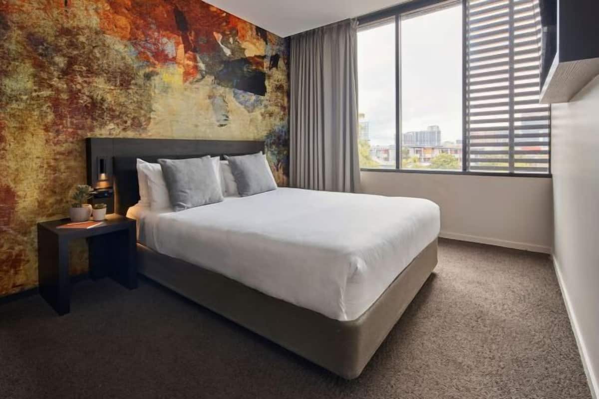 Ein modernes Hotelzimmer mit einem großen Bett, einem Nachttisch, einem Fenster mit Jalousien und einer strukturierten Wand.