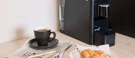 Una máquina de café, una taza de café, un periódico y un croissant sobre una mesa.