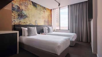 A hotel room with two beds, a large abstract mural on the wall, a window with curtains, and a view of the outside.