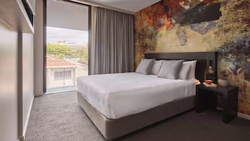 A modern hotel room with a large bed, a view of the city through a sliding door, and a textured wall.