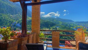 Una terraza con vistas a un paisaje montañoso, con pilares de ladrillo y plantas en macetas.