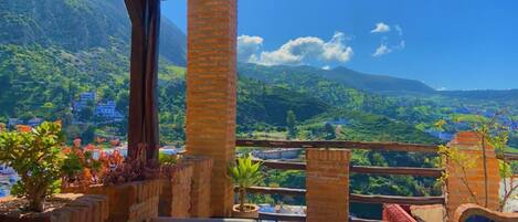 A terrace with a view of a mountainous landscape, featuring brick pillars and potted plants.
