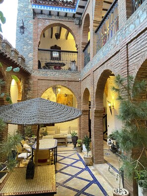 A courtyard with a central seating area, a staircase, and a balcony. - Riad Gharnata (Chefchaouen)