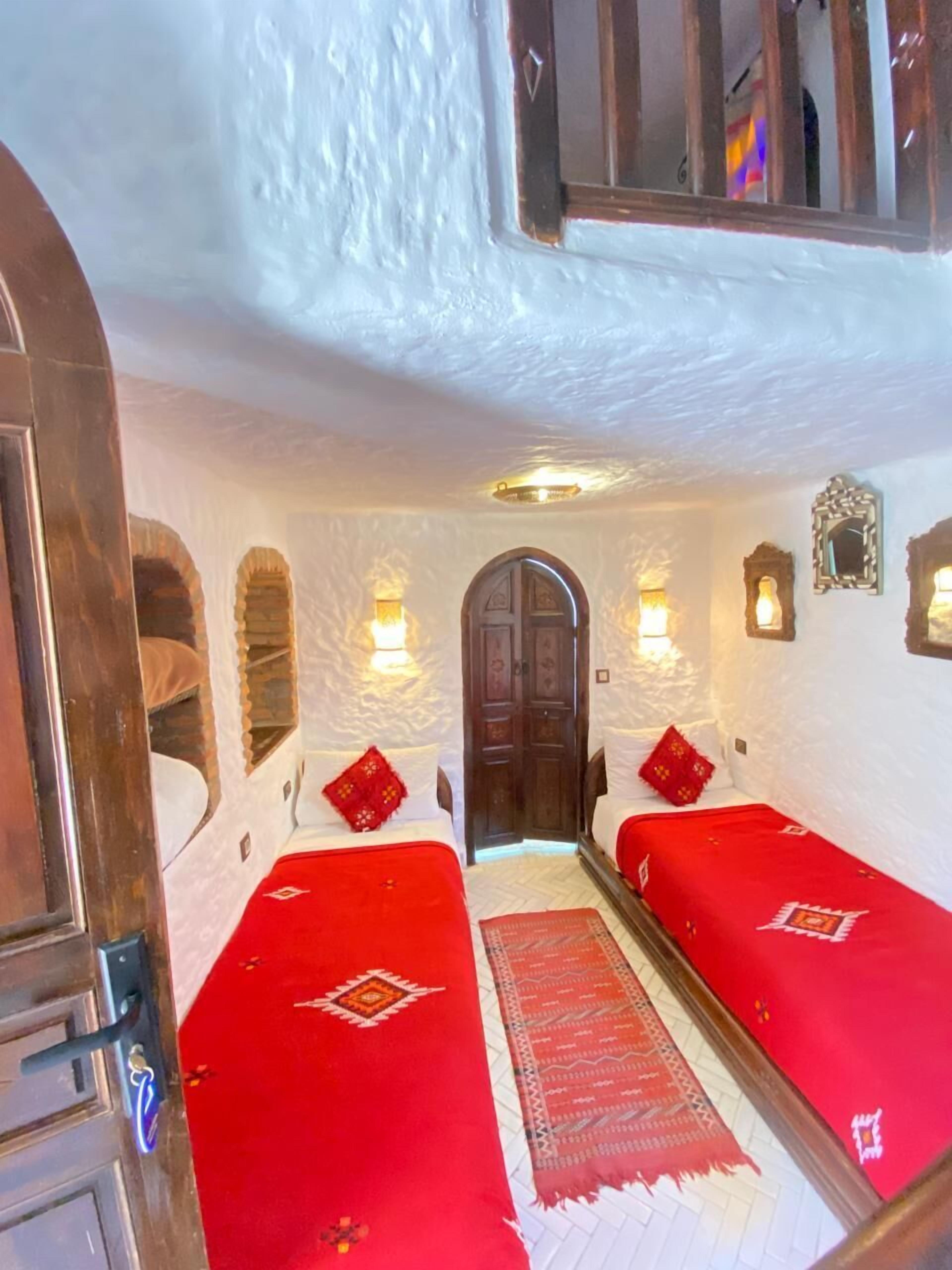 Habitació tradicional amb dos llits, una porta de fusta i una catifa vermella.