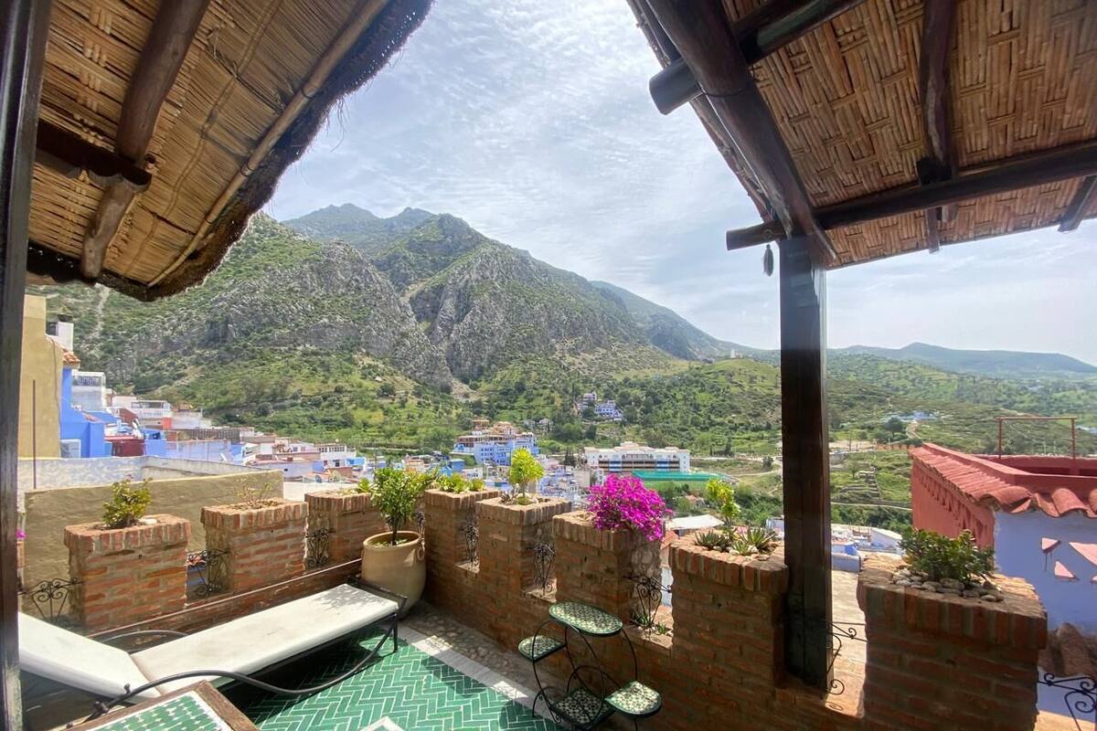 Terraço no telhado com paredes de tijolo, plantas em vasos e vista para uma paisagem montanhosa.